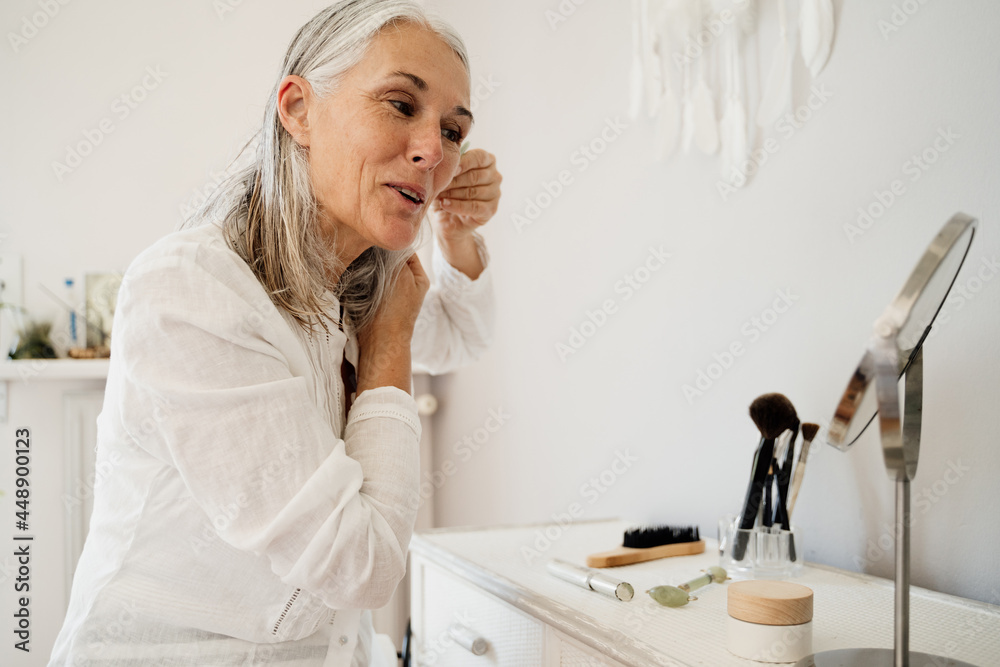Mature woman doing skin care in mirror at home Mature woman doing skin care in mirror at home