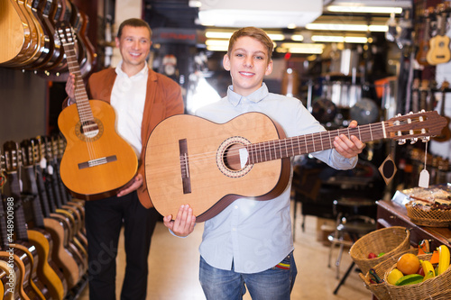 Happy young teenage boy and father choosing best acoustic guitar in musical shop