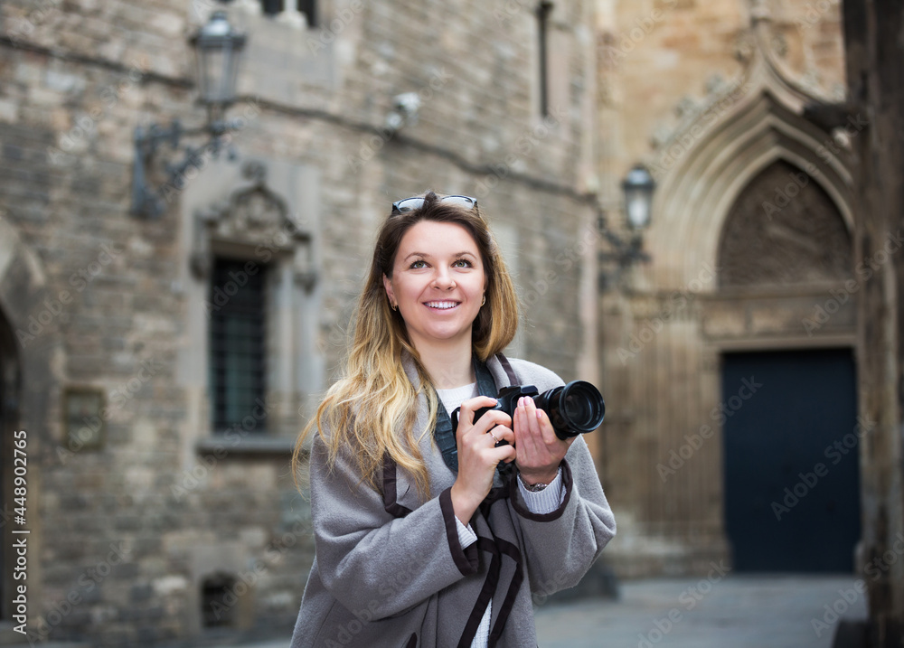 blond positive young girl holding camera in hands and photographing in the city