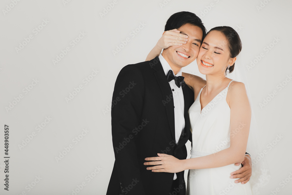 Young attractive Asian couple, bride and groom, woman wearing white wedding dress. Man wearing black tuxedo, standing arm in arm together in black and white. Concept for pre wedding photography Young attractive Asian couple, bride and groom, woman wearing white wedding dress. Man wearing black tuxedo, standing arm in arm together in black and white. Concept for pre wedding photography