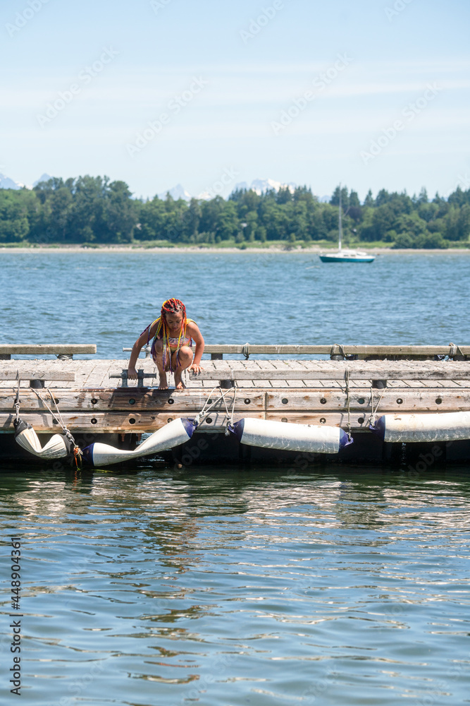 Girl crouches on edge of dock looking at water Girl crouches on edge of dock looking at water