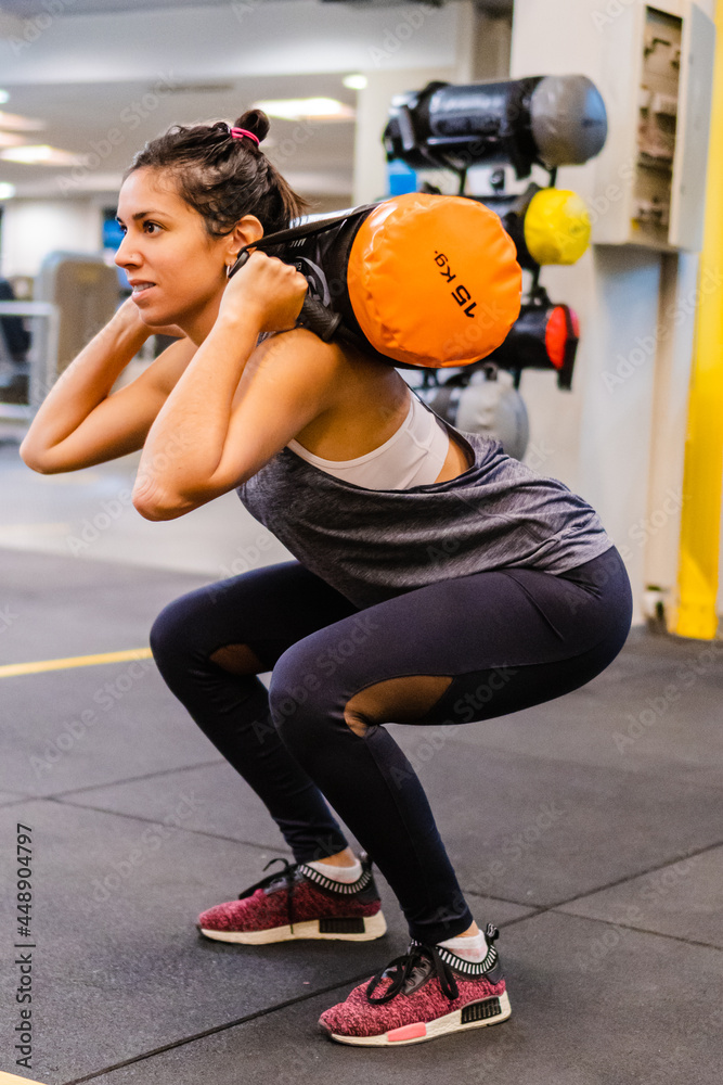 young hispanic latina woman in a gym doing squats with a core bag. vertical photo