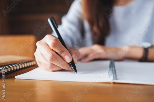 Closeup image of a woman writing on a blank notebook on wooden table