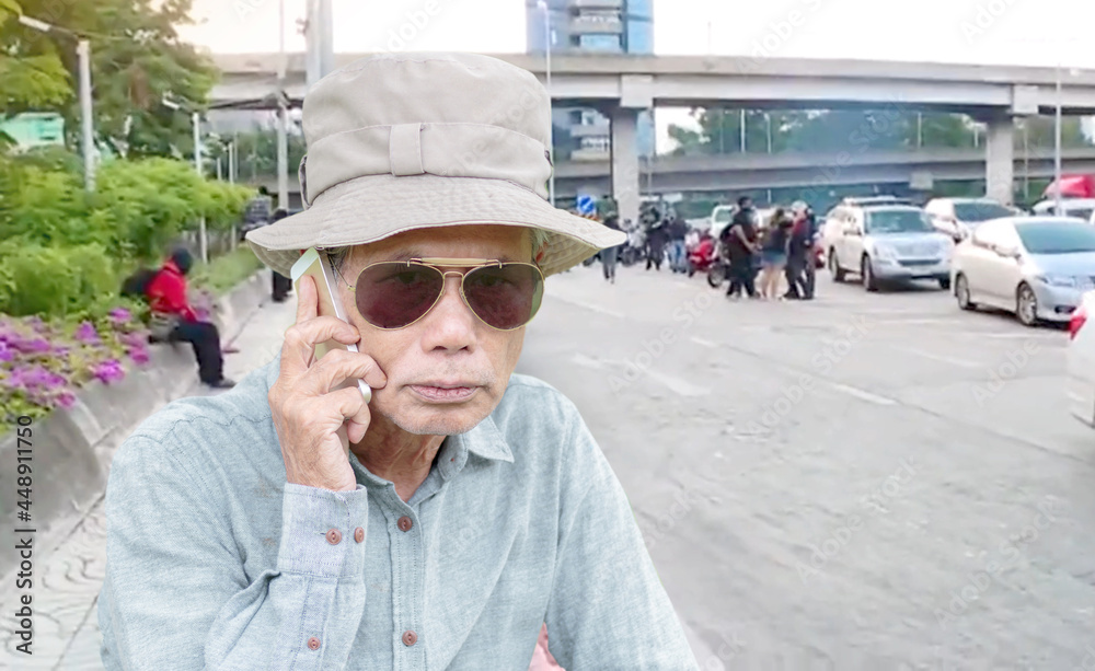 An elderly man wearing sunglasses uses a cell phone in a traffic-jammed city.