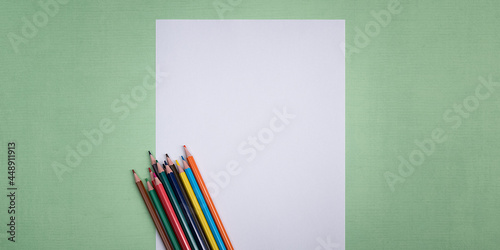 Fototapeta Naklejka Na Ścianę i Meble -  A blank white sheet and colored pencils for drawing on a plain textured background with space for copying and lettering.