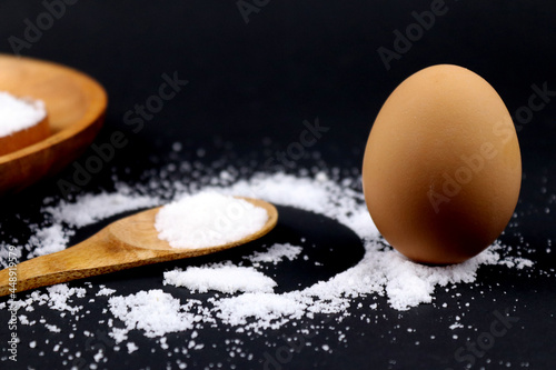 Standing egg on salt and wooden spoon in black background
