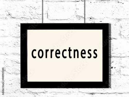Black frame hanging on white brick wall with inscription correctness