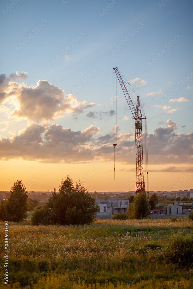A construction site with a high-rise block under construction in an urban environment dominated by a large industrial crane, silhouetted against a beautiful cloudy sunset. construction landscape A construction site with a high-rise block under construction in an urban environment dominated by a large industrial crane, silhouetted against a beautiful cloudy sunset. construction landscape
