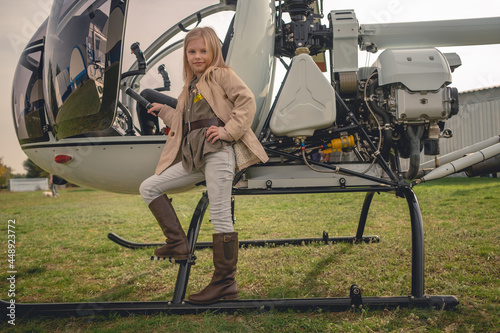 Blond preteen girl posing near open helicopter on flying field photo