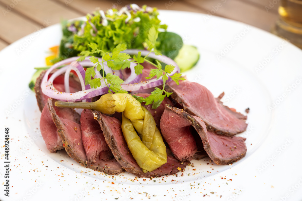 Roast beef slices with pepperoni, onions and salad on a white plate, copy space, selected focus