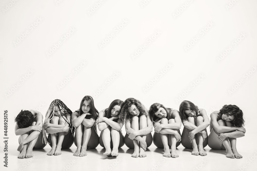 Naklejka premium Girls with different types in one photo. The girls sit on the floor and hug themselves by the legs. A place for a text on female psychology. Understanding Female Psychology