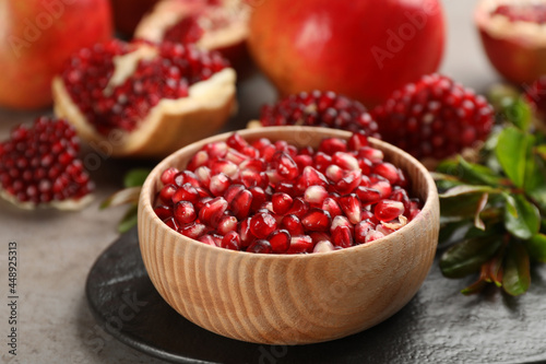Delicious ripe pomegranate kernels in bowl on grey table, closeup