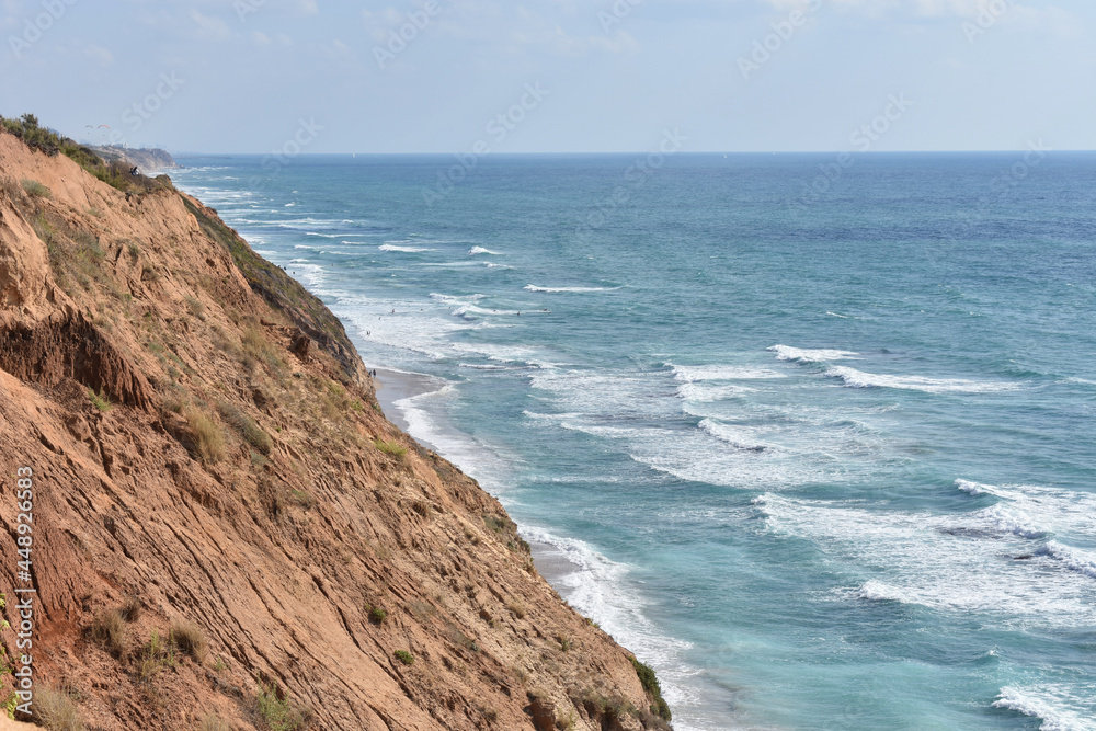 Top view of a sandy cliff and turquoise sea with waves.