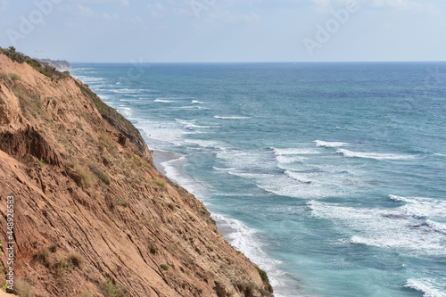 Photos Top view of a sandy cliff and turquoise sea with waves.