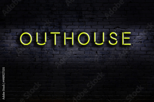 Night view of neon sign on brick wall with inscription outhouse