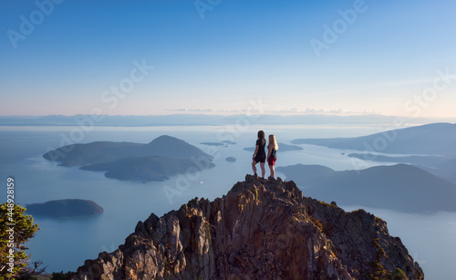 Adventurous Caucasian Woman Friends Hiking on top of a Rocky Mountain Cliff. Sunny Summer Sunset. Mnt Brunswick Hike  North of Vancouver  British Columbia  Canada.