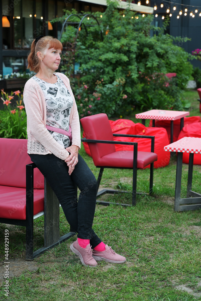 portrait of a red-haired adult woman standing alone in a summer cafe