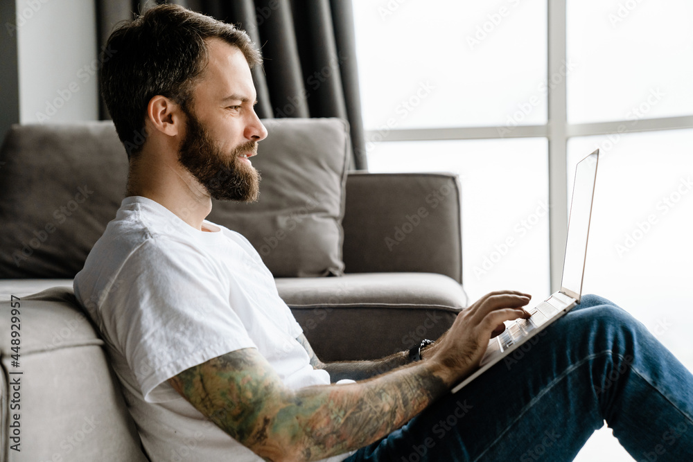 Bearded european man working with laptop while sitting on floor