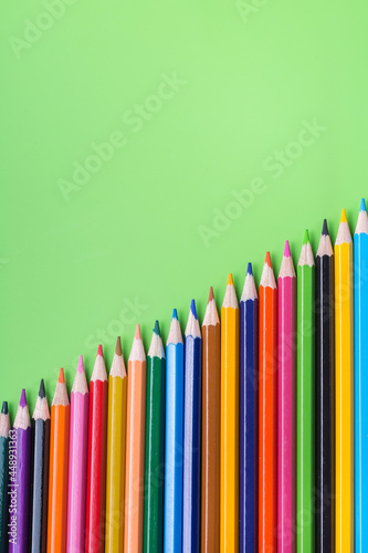 Colourful rainbow pencils and alarm clock on lime green background