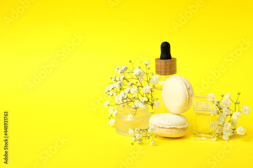 Cosmetics, macaroons and flowers on yellow background