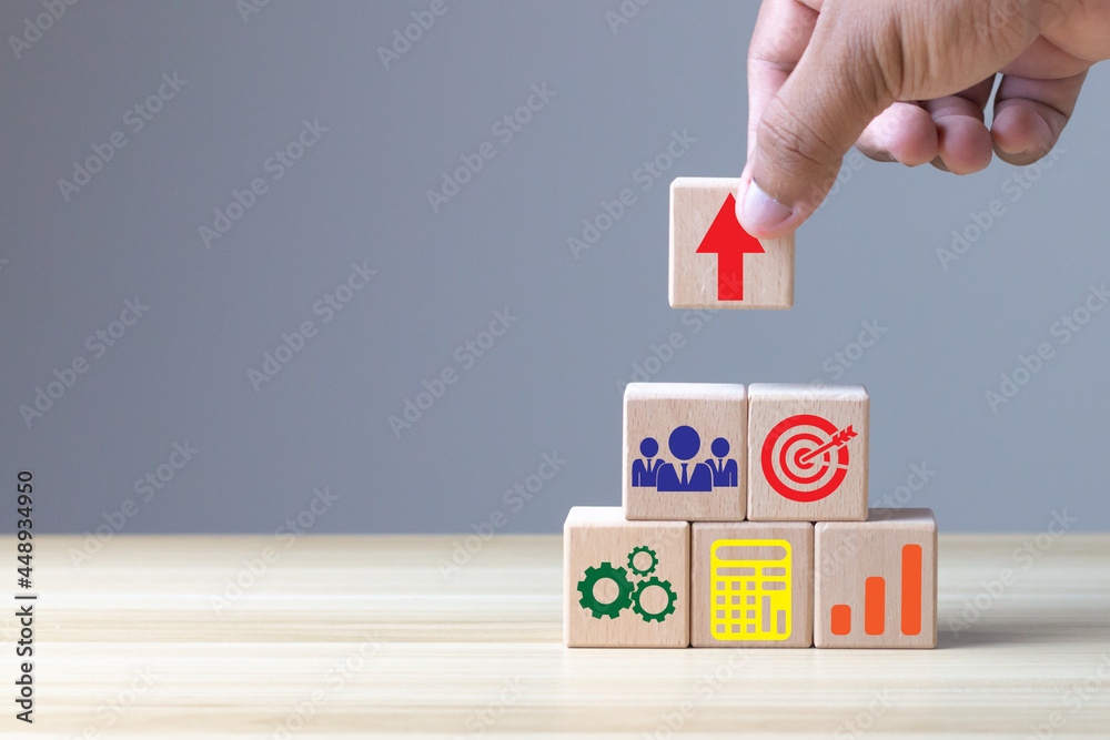 Hand arranging wood block stacking with icon arrow and business, targeting the business concept. The economy is improving. Hand arranging wood block stacking with icon arrow and business, targeting the business concept. The economy is improving.