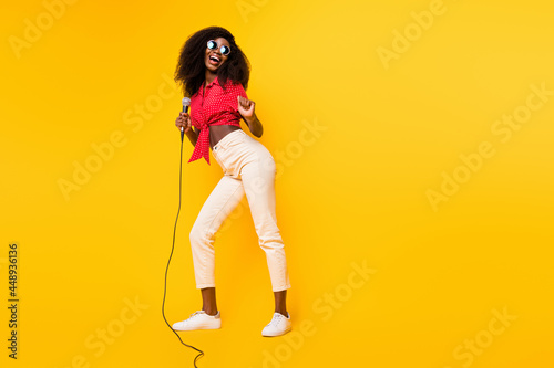 Full size photo of nice optimistic brunette lady sing look empty space wear red top eyewear isolated on yellow backgound