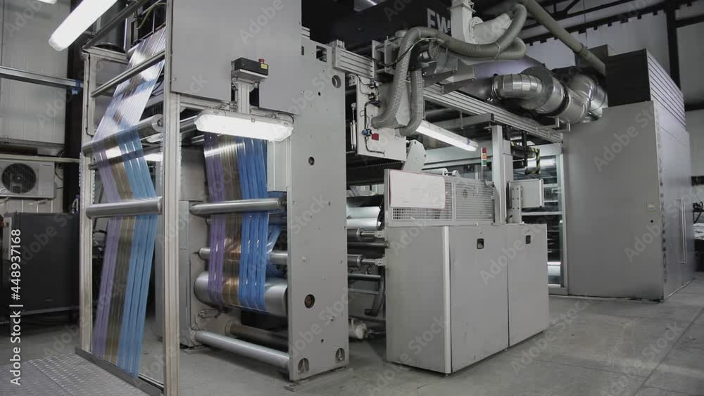 A large machine for printing on packaging works at the factory. The factory produces packaging. The machine applies a drawing on the packaging made of paper, glass, plastic and other things. A large machine for printing on packaging works at the factory. The factory produces packaging. The machine applies a drawing on the packaging made of paper, glass, plastic and other things.