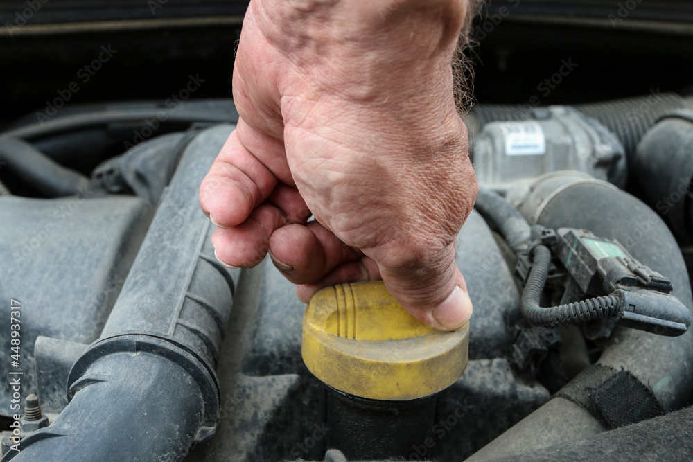 The man unscrews the oil cap on the car's engine.