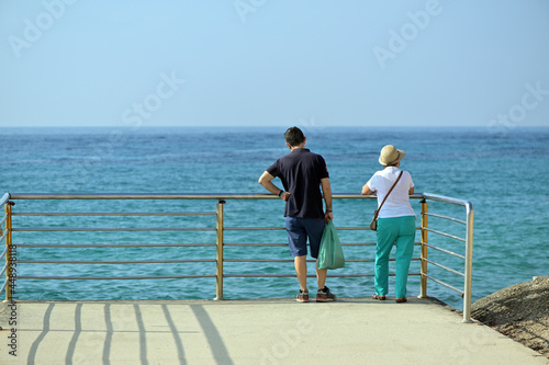 An elder love couple looks to the sea in front of a protection grid in Finestrat-Spain.