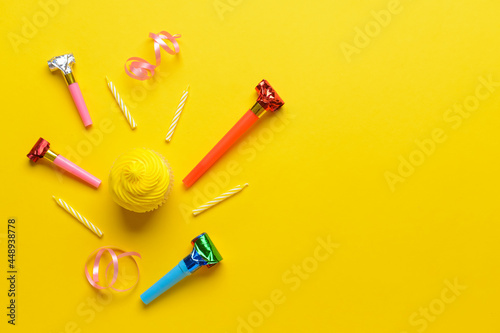 Tasty Birthday cupcake with candles, ribbons and party whistles on color background
