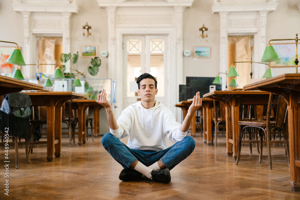 Young middle eastern man meditating while sitting on floor at library
