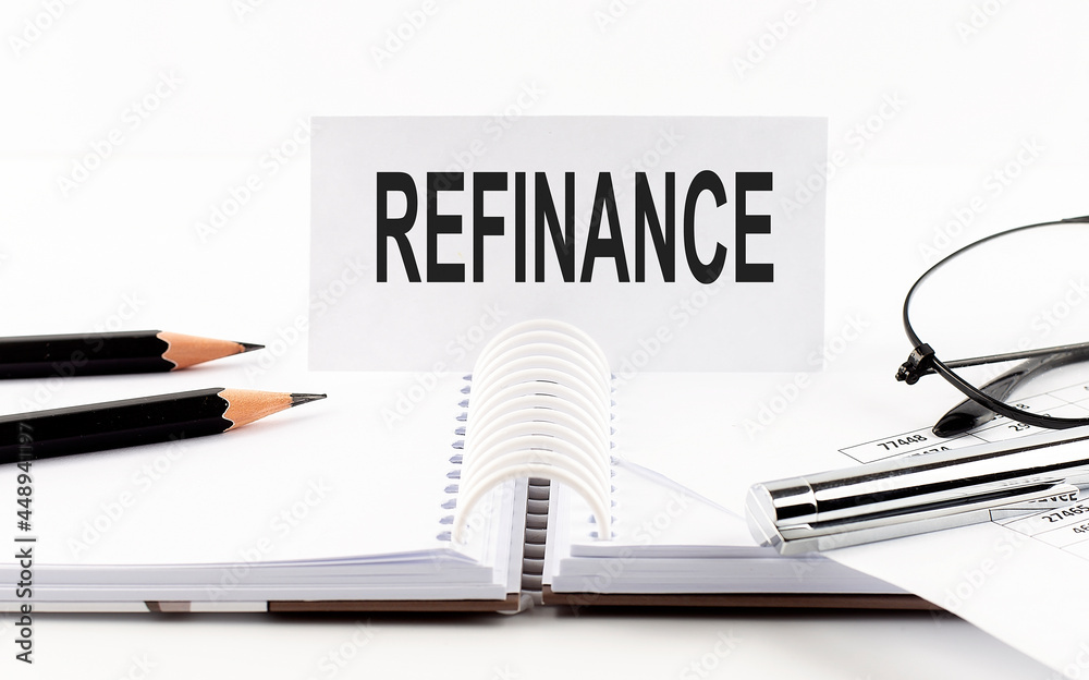 Text REFINANCE on paper card,pen, pencils, glasses,financial documentation on table - business concept Text REFINANCE on paper card,pen, pencils, glasses,financial documentation on table - business concept