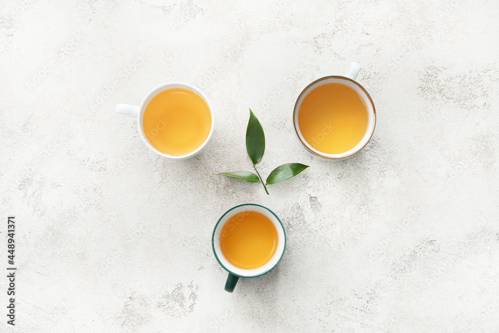 Cups of tea and green leaves on light background Cups of tea and green leaves on light background