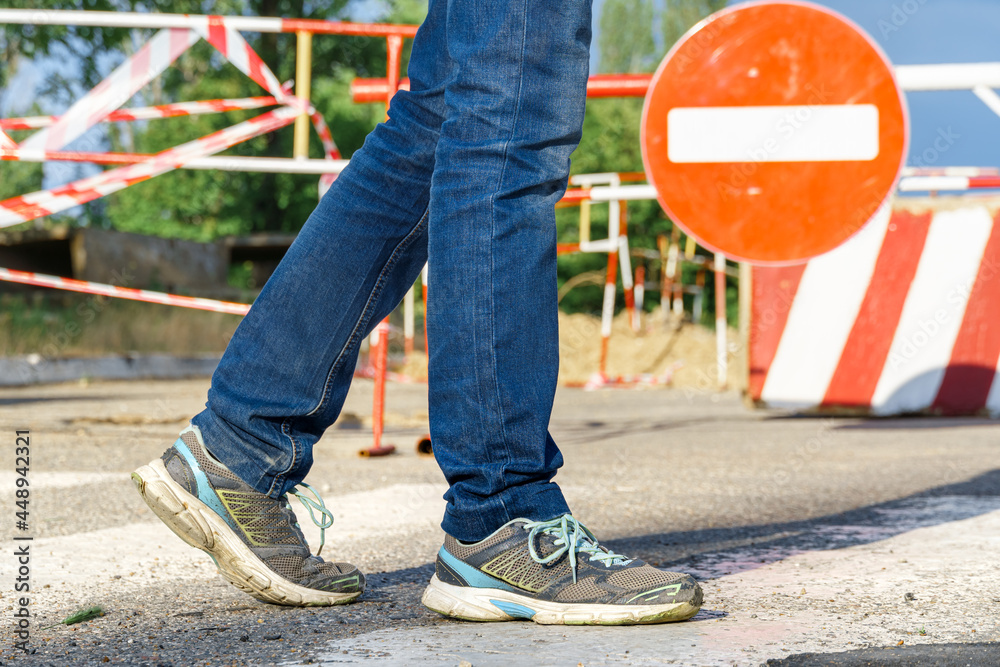 a pedestrian walks along a pedestrian crossing next to the road sign - traffic is prohibited and road works, the road is closed for maintenance a pedestrian walks along a pedestrian crossing next to the road sign - traffic is prohibited and road works, the road is closed for maintenance