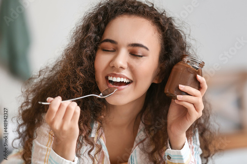 Young African-American woman eating chocolate paste in kitchen