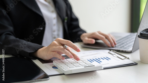 Close-up of businesswoman using calculator to do accounting calculations with laptop and graphing at office.