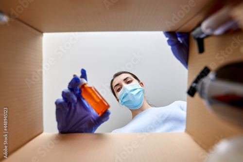 home delivery, shipping and pandemic concept - woman in protective medical mask and gloves unpacking parcel box with cosmetics and beauty products