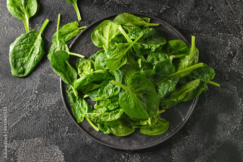 Plate with fresh spinach leaves on dark background
