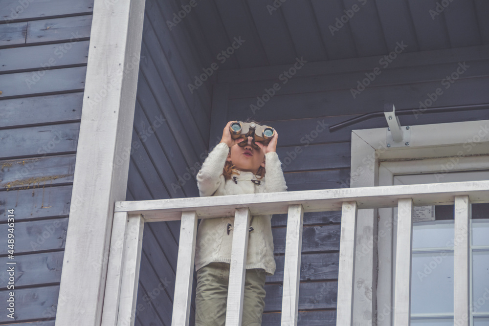the child girl looks through binoculars standing on the balcony of the house