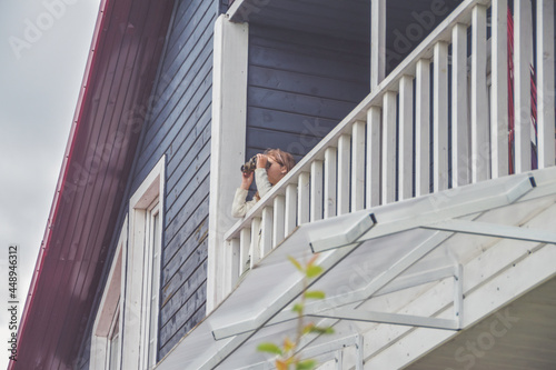 the child girl looks through binoculars standing on the balcony of the house