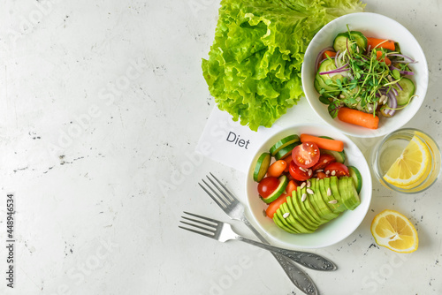 Bowls with delicious vegetable salad and paper sheet with word DIET on light background