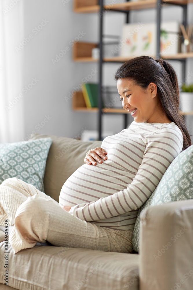 pregnancy, rest, people and expectation concept - happy smiling pregnant asian woman sitting on sofa at home pregnancy, rest, people and expectation concept - happy smiling pregnant asian woman sitting on sofa at home