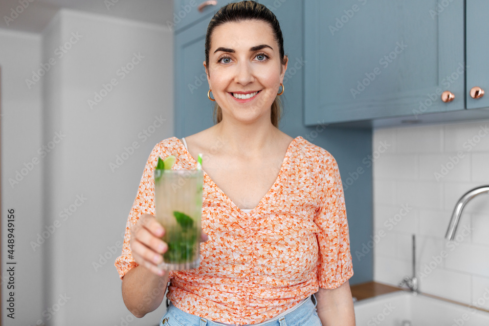 culinary, drinks and people concept - happy smiling young woman holding glass of lime mojito cocktail at home kitchen culinary, drinks and people concept - happy smiling young woman holding glass of lime mojito cocktail at home kitchen