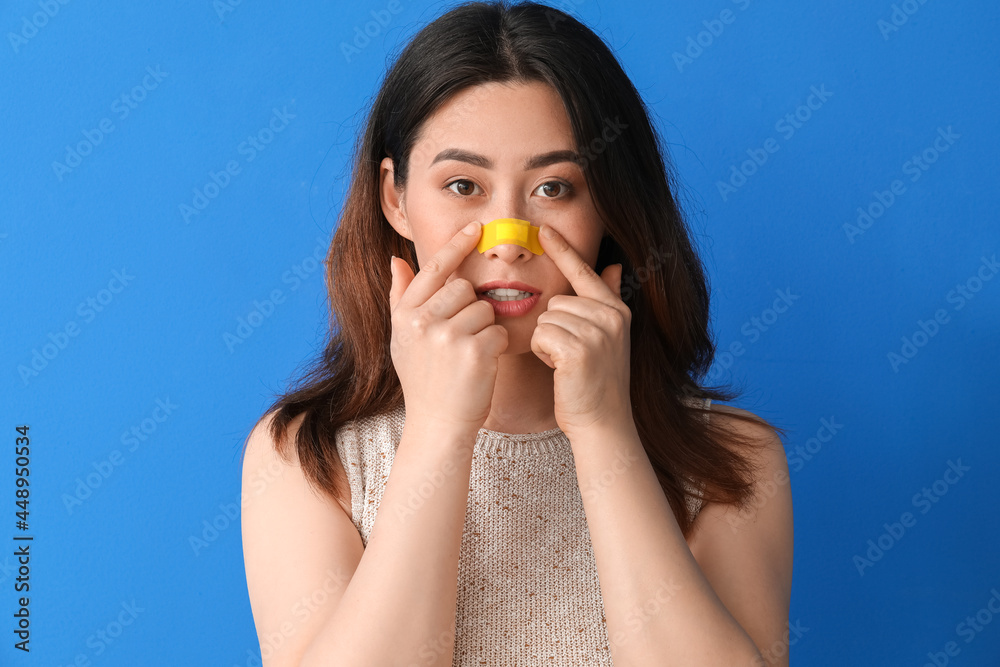 Young Asian woman with applied medical patch against color background Young Asian woman with applied medical patch against color background