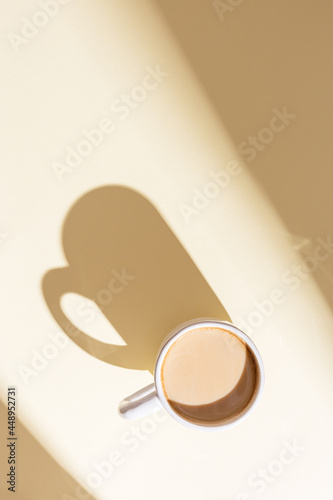 Cup of coffee with milk on beige with sunlight. Breakfast on sunny summer day.