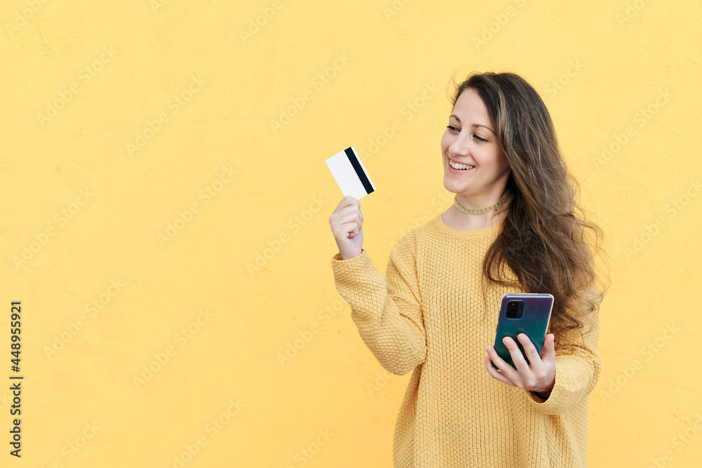 Laughing young woman using cell phone with bank credit card in hand Laughing young woman using cell phone with bank credit card in hand