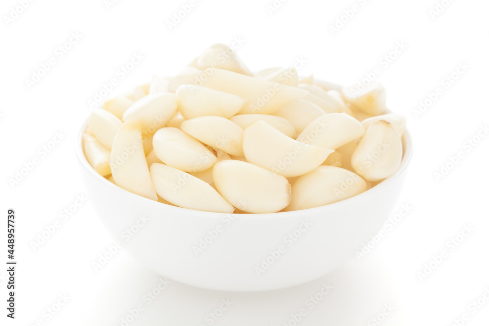 Close-Up of organic fresh peeled garlic (Allium sativum) in white ceramic bowl over white background Close-Up of organic fresh peeled garlic (Allium sativum) in white ceramic bowl over white background
