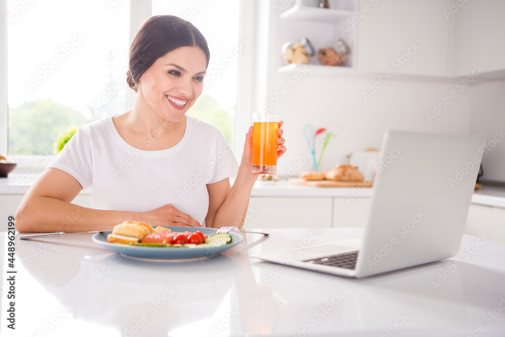 Photo of positive happy mature woman smile watch video laptop drink juice eat meal indoors inside kitchen