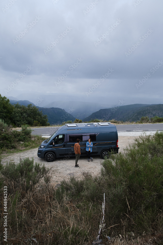 Young couple traveling in a van standing on the side of a road with beautiful views.