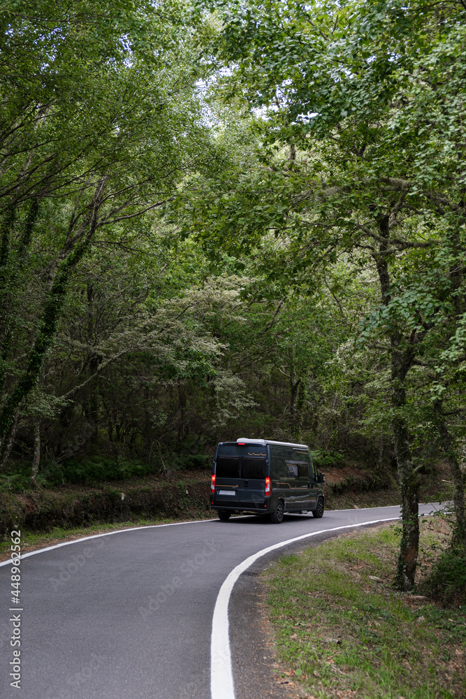 Camper van driving through a green forest. Vertical photo.